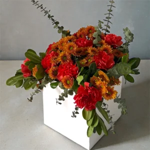 Autumn Ember floral arrangement with red carnations, bronze chrysanthemums, and fresh greenery in a white square box