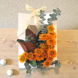 Orange chrysanthemum floral arrangement with eucalyptus in an elegant white gift box